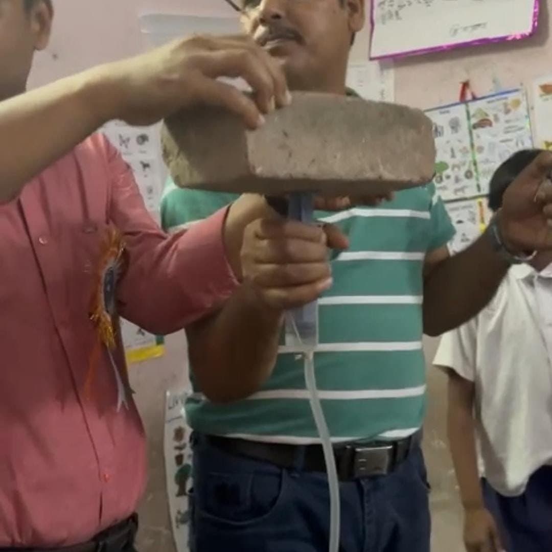 A facilitator holding up a heavy stone slab attached by a tube to a suction device, with students watching from either side.
