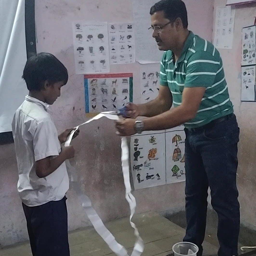 A facilitator and a school student together holding a long loop of paper that has been cut along its length.
