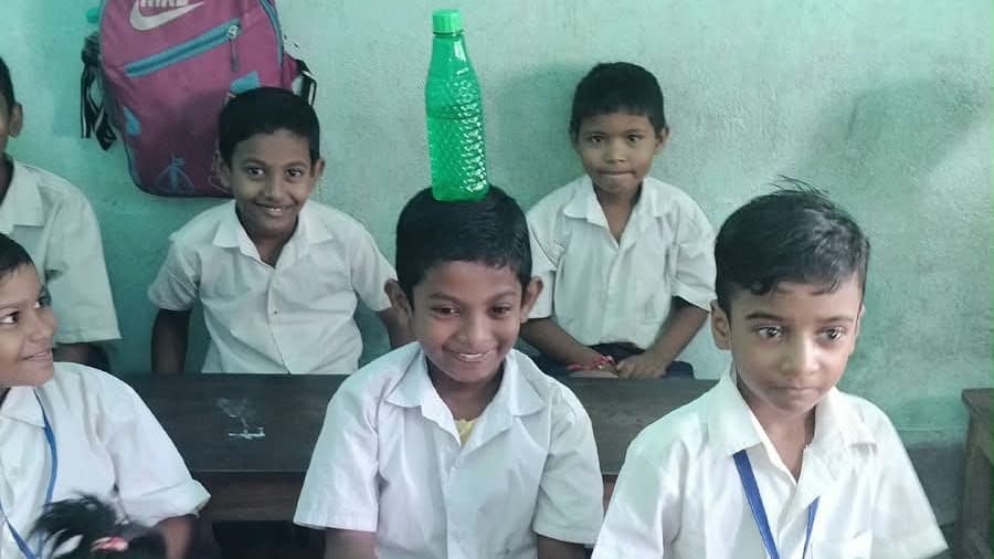 Four school students in white uniforms seated at a desk, smiling towards the camera during a session.