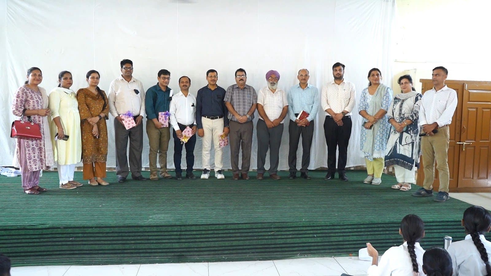 Facilitators and school staff standing across a stage at the end of a session.