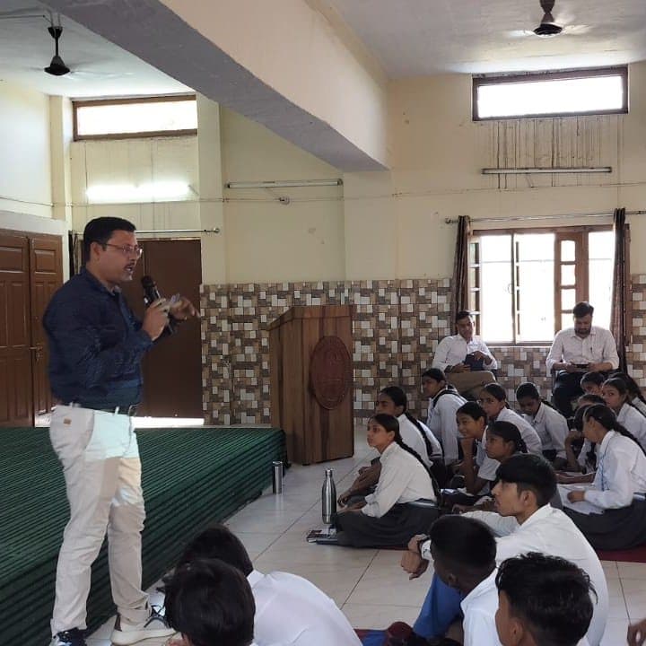 A facilitator speaking into a microphone while students sit on the floor around him.