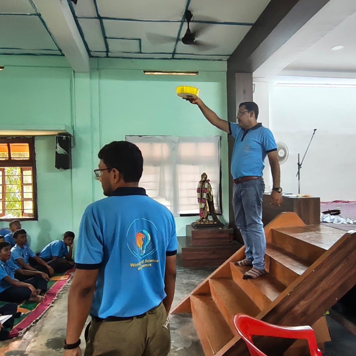 A facilitator holding a yellow funnel above his head for the room to see, students seated below.