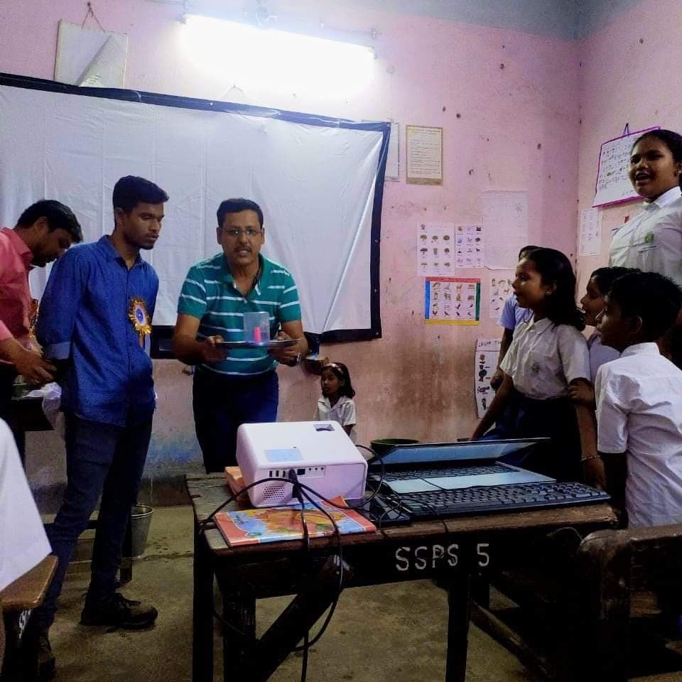 Facilitators setting up a projector on a table in a pink-walled classroom as students look on.