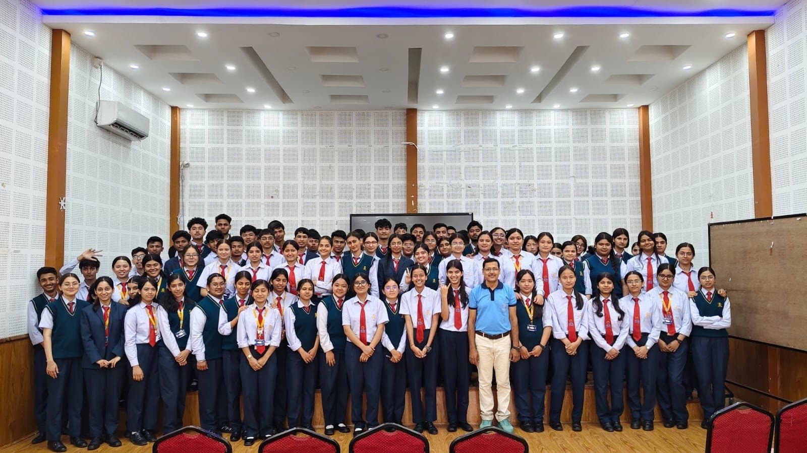 A large group photograph of students and staff arranged across the front of a school hall.