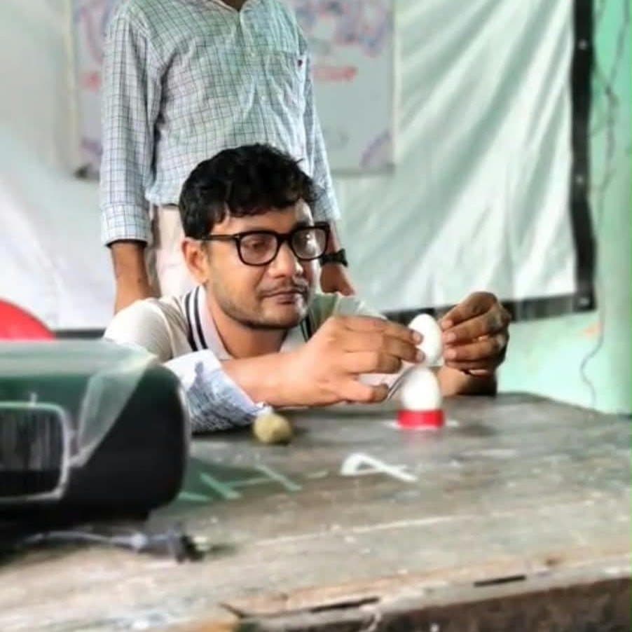 A young man concentrating as he assembles small apparatus on a wooden table.