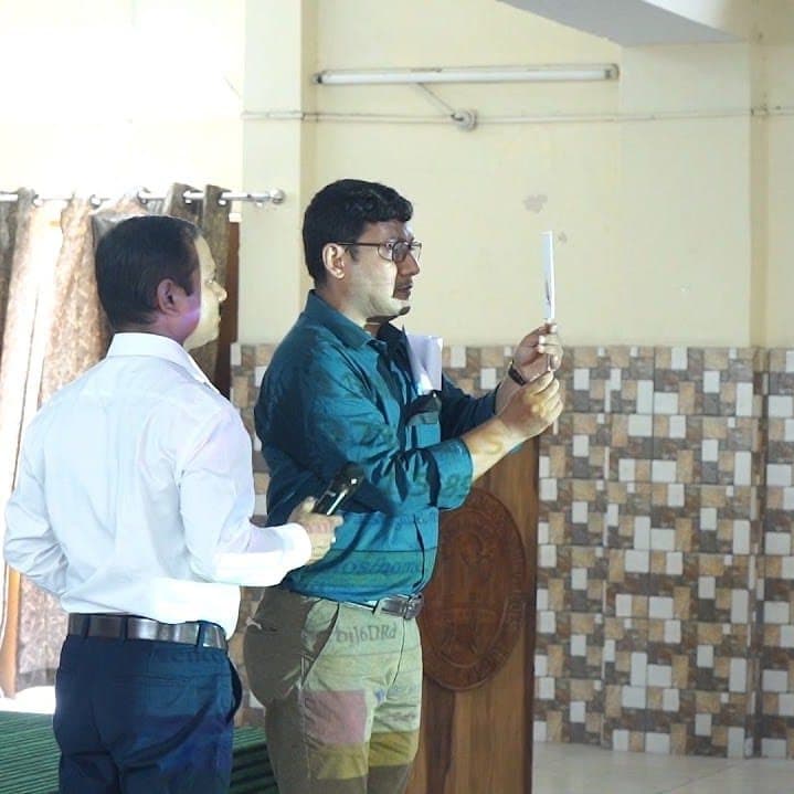 Two facilitators beside a lectern, one holding a small object up for the room to see.