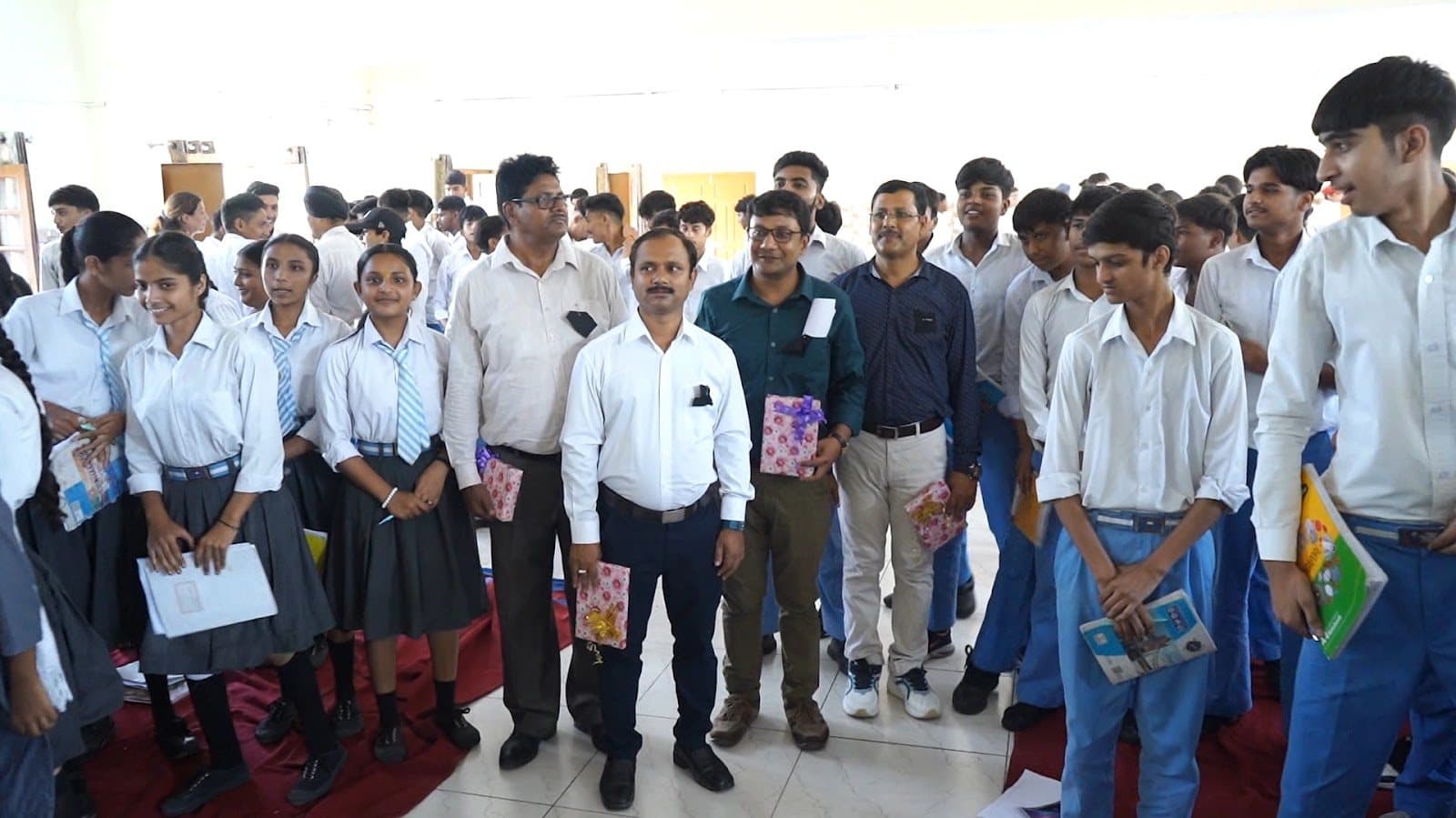 A dense crowd of students in white uniforms with facilitators standing among them.