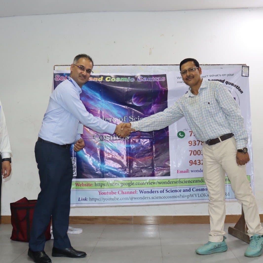 Two men shaking hands in front of a printed WSCosmos banner listing the initiative's website and YouTube channel.