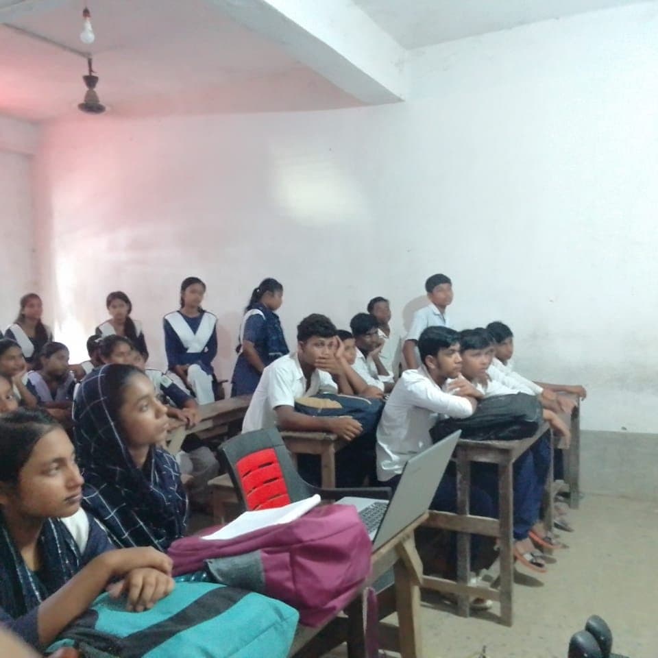 Students at desks in a classroom, one in the foreground listening.