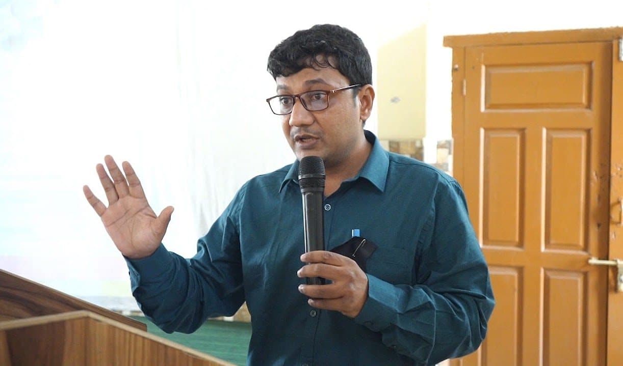 A facilitator speaking into a microphone with one hand raised.