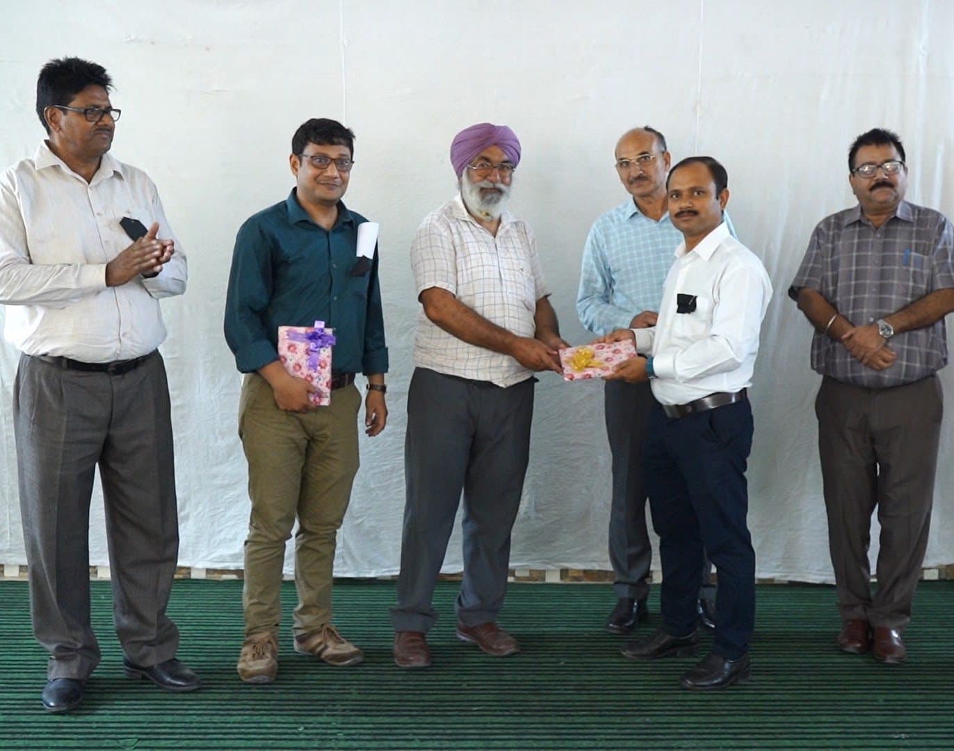 A man being presented with a wrapped memento by school staff on a stage.