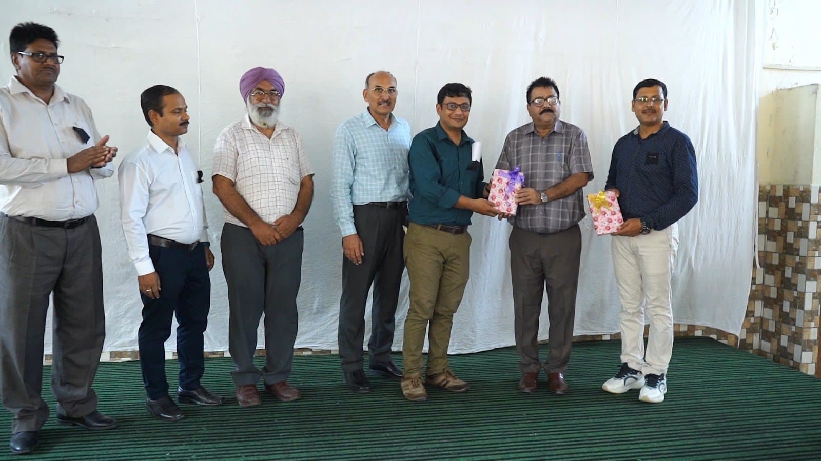 A line of men on a stage, one receiving a wrapped memento.