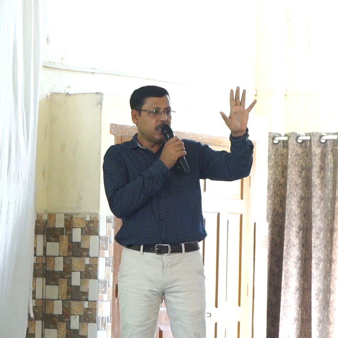 A speaker mid-sentence with a microphone, one hand raised.