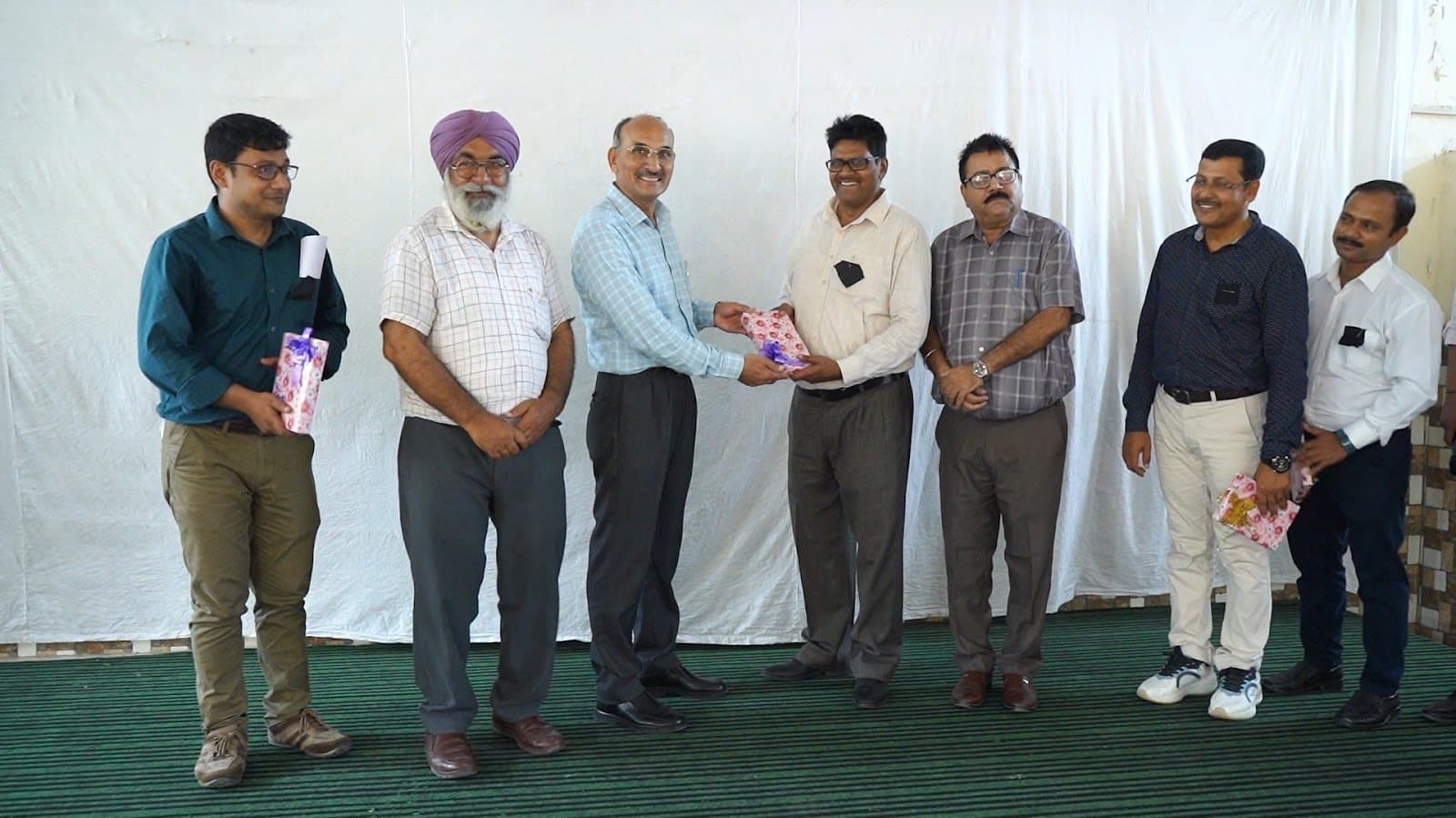 A line of facilitators and school staff on a stage, one presenting a wrapped gift.