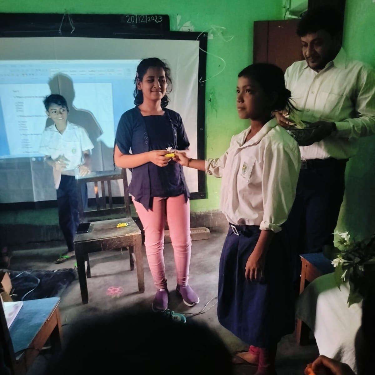 A facilitator guiding two students through a small hand-held demonstration in front of a projector screen.