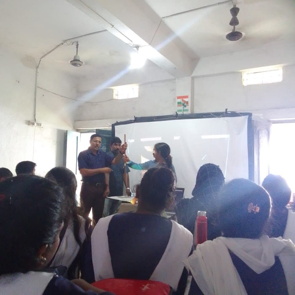 Students seen from behind watching a facilitator demonstrate with a light source in a darkened classroom.