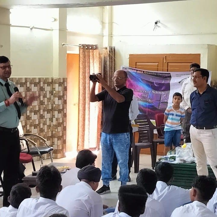 A man photographing proceedings in a room with a WSCosmos banner and students seated on the floor.