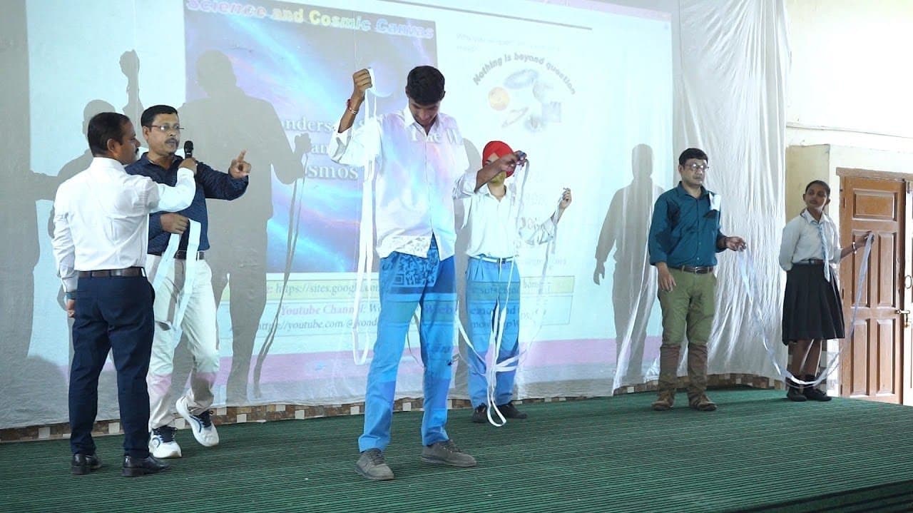 Facilitators and students on a stage holding long paper strips, a projected slide behind them.