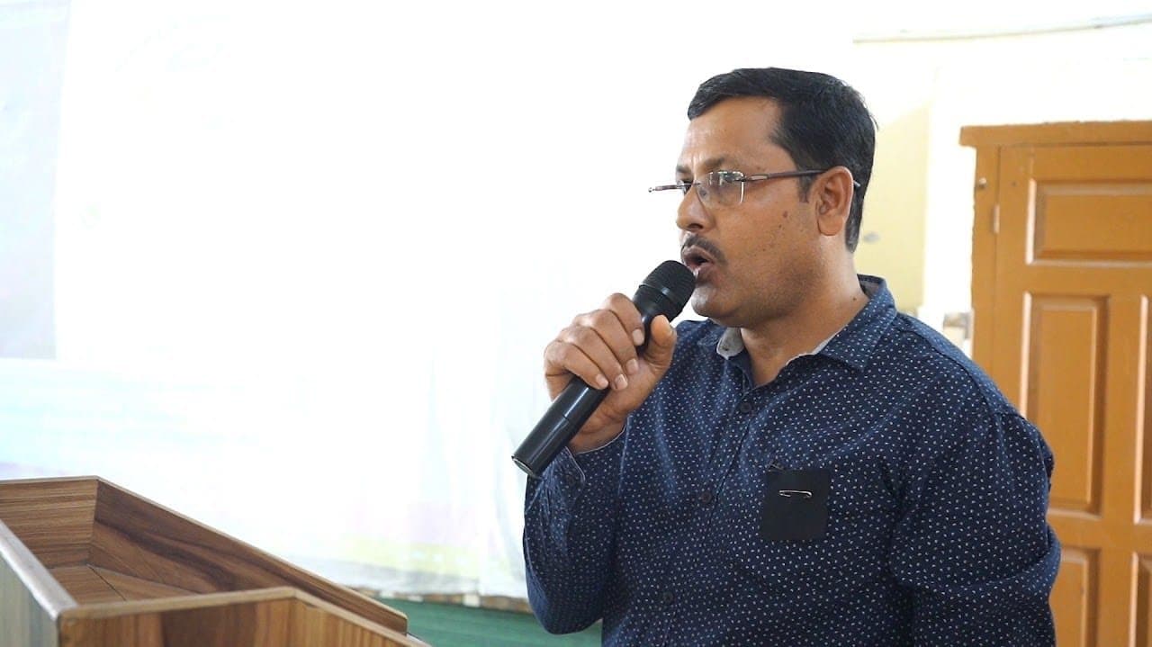 A facilitator speaking into a microphone beside a lectern.