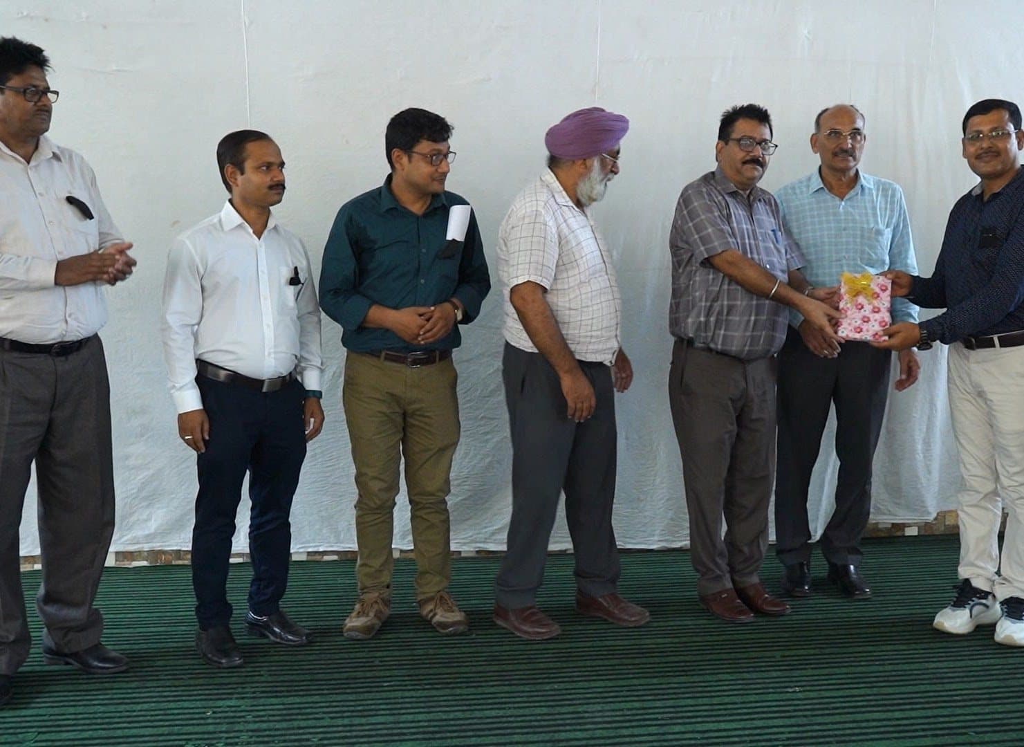 A line of men standing across a stage as one is presented with a wrapped gift.