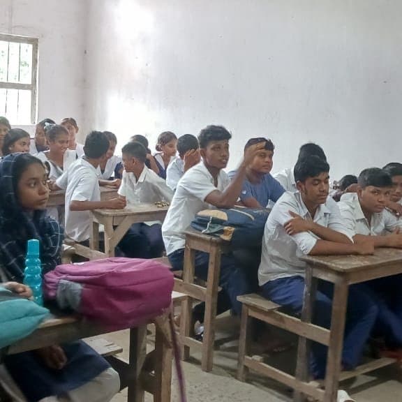 Students at wooden desks in a classroom looking towards the front of the room.