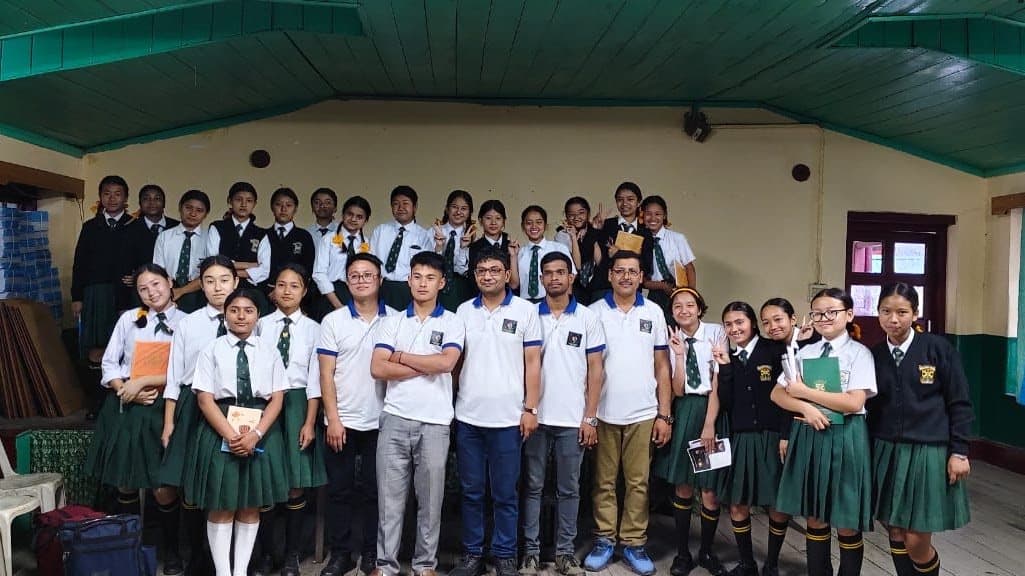 A group photograph of students in green and white uniforms with facilitators in a school hall.