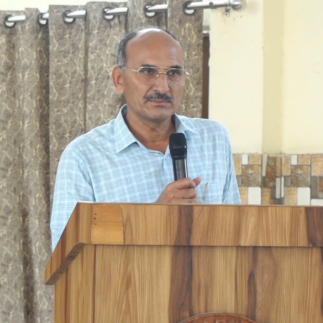 A senior teacher speaking into a microphone from a wooden lectern.